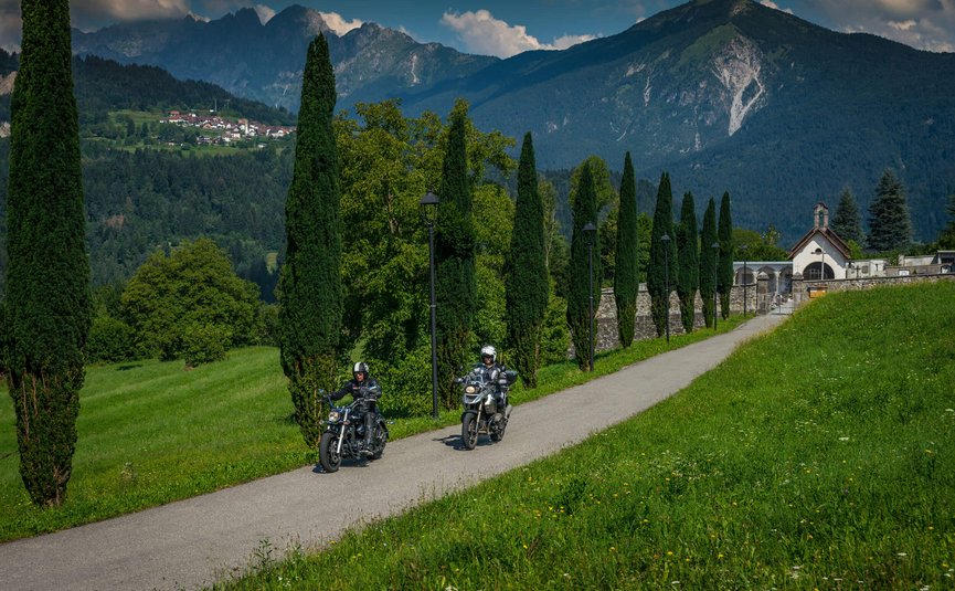 Motorradurlaub in Friaul – Julisch Venetien © Moppetfoto.de Zwei Motorradfahrer fahren auf einem Weg mit Bäumen und Bergen im Hintergrund