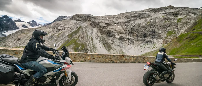 Reschensee – Stilfserjoch – Vinschgau © Moppetfoto.de Zwei Motorradfahrer auf Bergstraße unter wolkigem Himmel