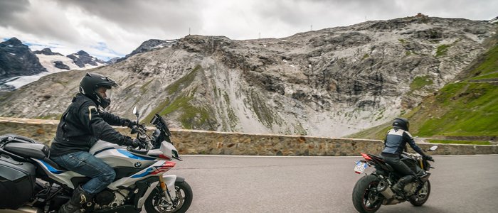 Zwei Motorradfahrer auf Bergstraße unter wolkigem Himmel