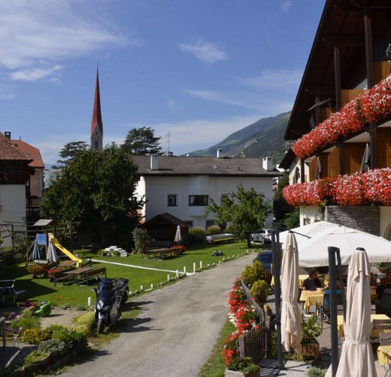 Dorf mit Altbau, Blumenbalkonen und Außenrestaurant an sonnigem Tag