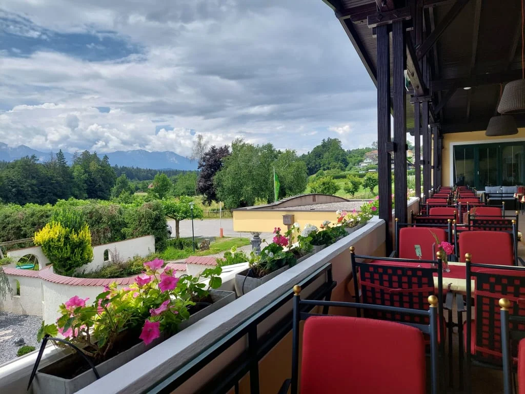 Balkon mit roten Stühlen und Blumen mit Blick auf grüne Landschaft und Berge