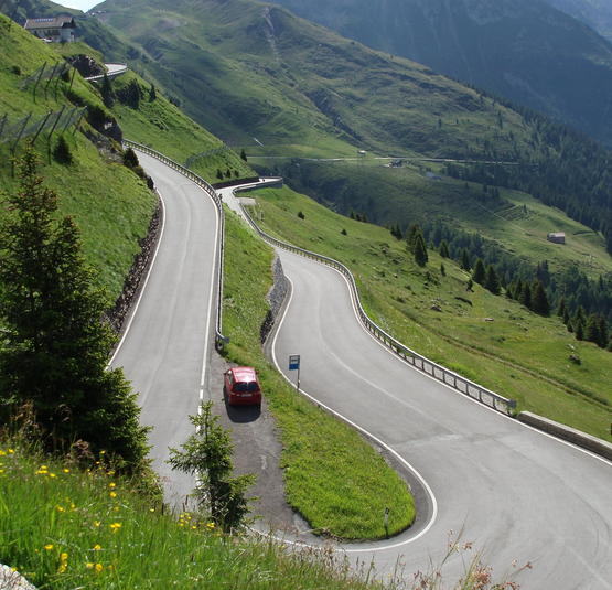 Serpentinenstraße mit rotem Auto in grüner Berglandschaft
