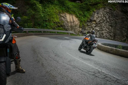 Motorcyclists riding a winding mountain road with rock walls and greenery