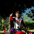 Michele Acler © Andrea Acler Mann mit Motorradkleidung zeigt Daumen hoch neben rotem Motorrad im Freien