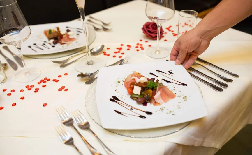 Hand placing gourmet dish with ham and garnish on set dining table