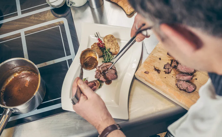 Chef plating meat with sauce on a plate in professional kitchen