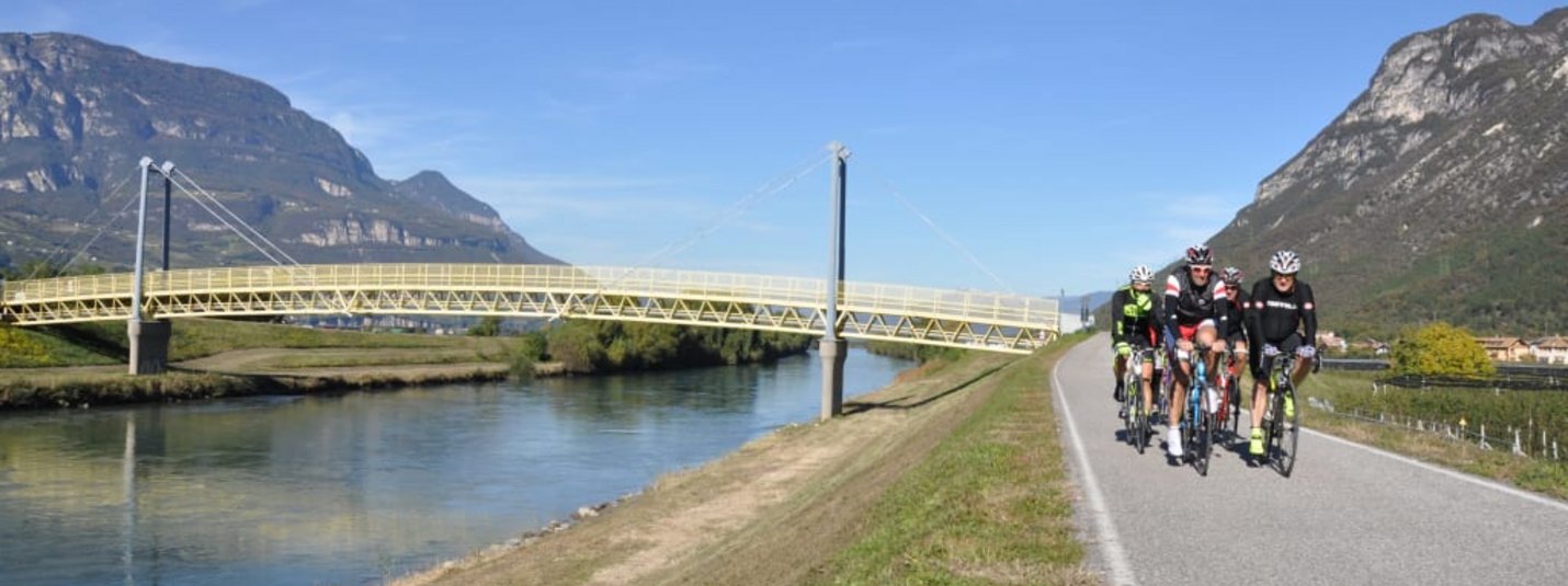 Gruppe Radfahrer auf Weg neben Fluss und Brücke in bergiger Landschaft