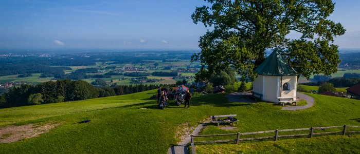 Motorradurlaub in Bayern © Moppetfoto.de Berglandschaft mit Kapelle, Baum und Menschen bei Motorrollern
