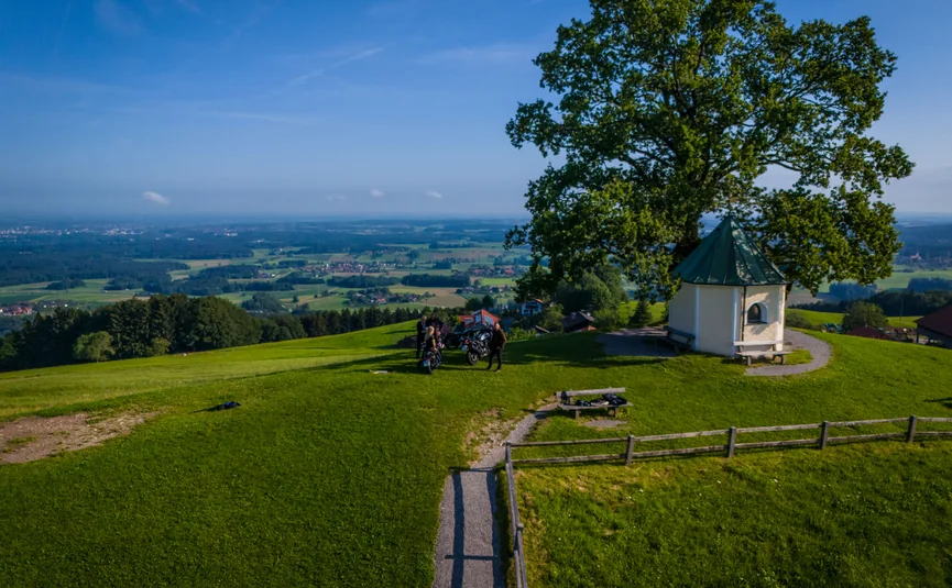 Hill landscape with chapel, tree, and people with scooters