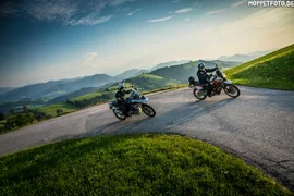 Zwei Motorradfahrer auf kurviger Bergstraße bei sonnigem Wetter