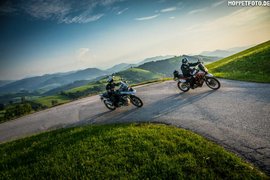 Two motorcyclists riding on a winding mountain road in sunny weather