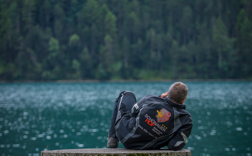 Person liegt entspannt auf einem Steinblock am Seeufer vor Wald