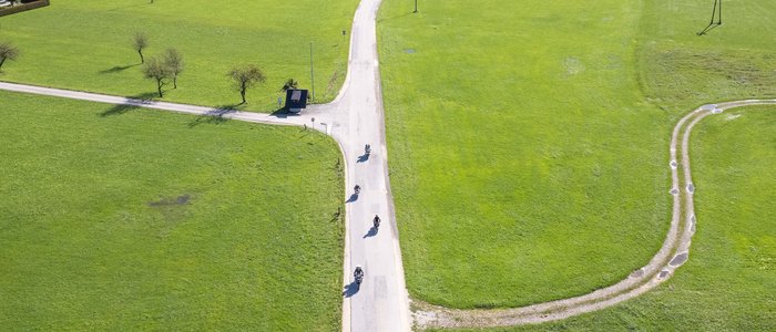 Luftaufnahme von einem langen Landstraße mit Radfahrern durch grüne Wiesen