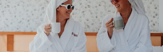 Zwei Frauen in Bademänteln und Handtüchern trinken Kaffee im Bett