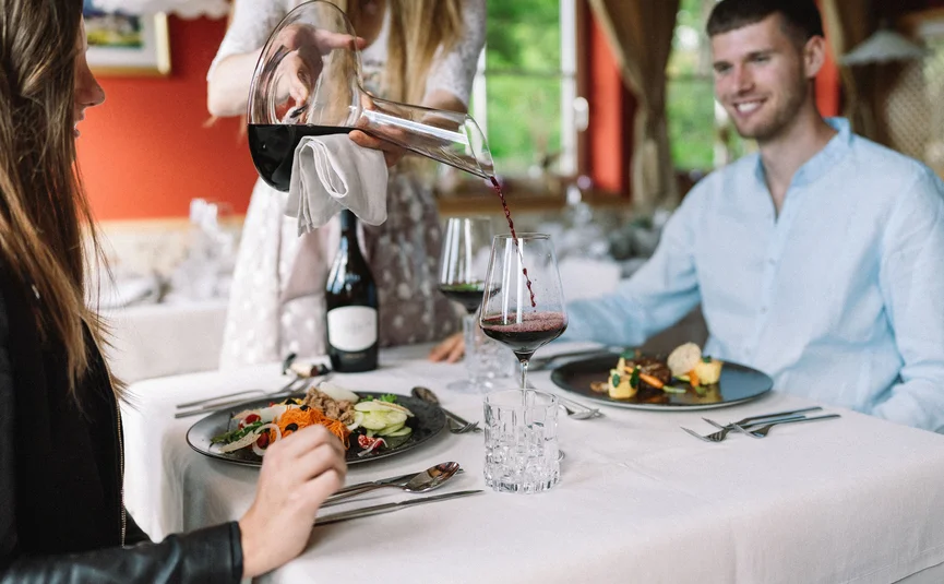 Person pouring red wine into a glass at a meal