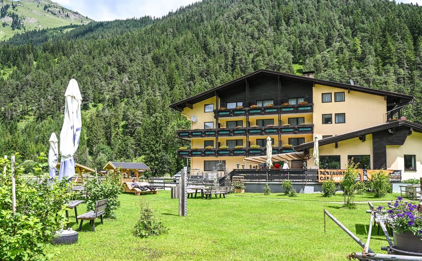 Gelbes Alpenhotel mit Garten vor bewaldetem Berg im Sommer