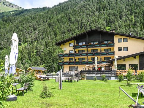 Geel alpenhotel met tuin en beboste berg op de achtergrond in de zomer