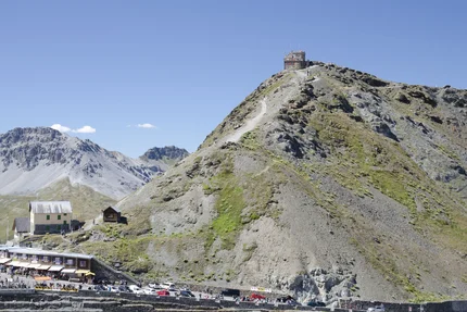 Mountain with path and building on top, cars and people at the bottom