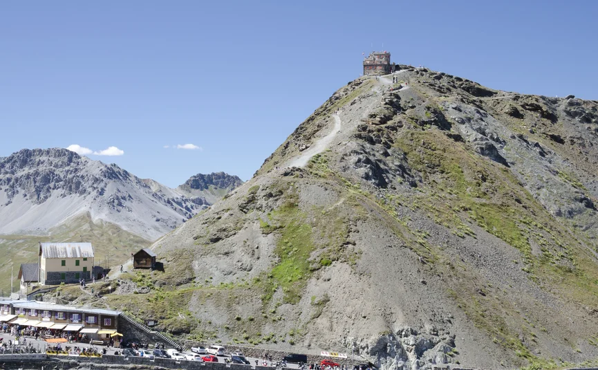 Stelvio Pass Mountain with path and building on top, cars and people at the bottom