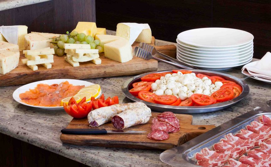 Assorted cheese, salami, tomatoes, mozzarella, and salmon on a buffet table