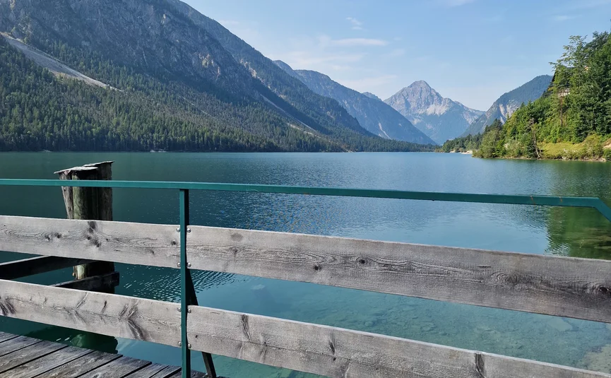 Wooden pier on clear mountain lake with view of mountains under blue sky