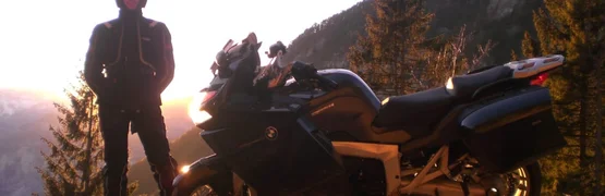Person mit Helm neben einer schwarzen BMW-Motorrad bei Sonnenuntergang in den Bergen