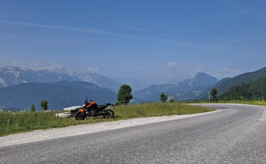 Motorrad geparkt neben einer Bank auf Bergstraße mit Alpenblick