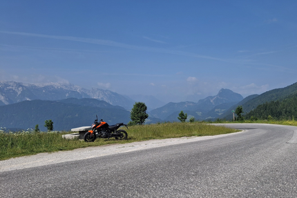 Motorrad geparkt neben einer Bank auf Bergstraße mit Alpenblick
