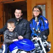 Family with child poses by blue Honda motorcycle in front of wooden house