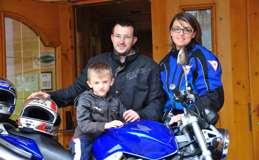 Family with child poses by blue Honda motorcycle in front of wooden house