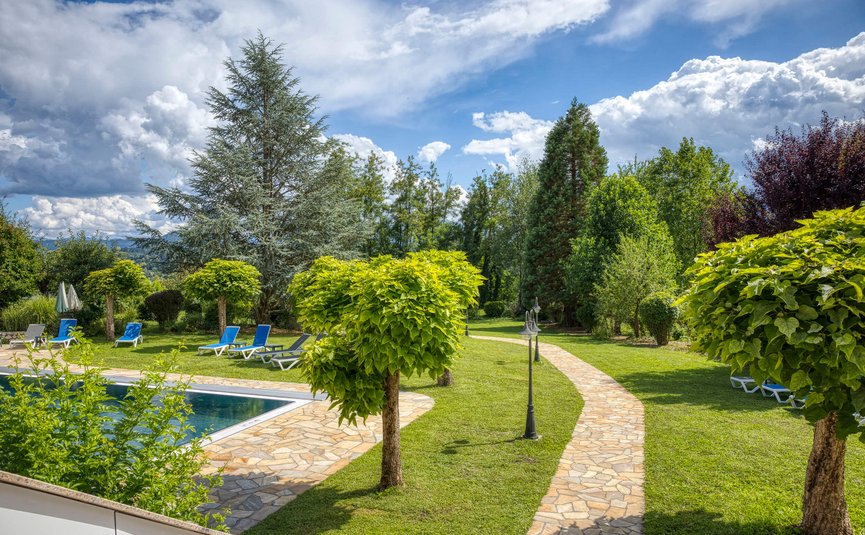 Garten mit Pool, Liegestühlen und Weg unter einem bewölkten Himmel