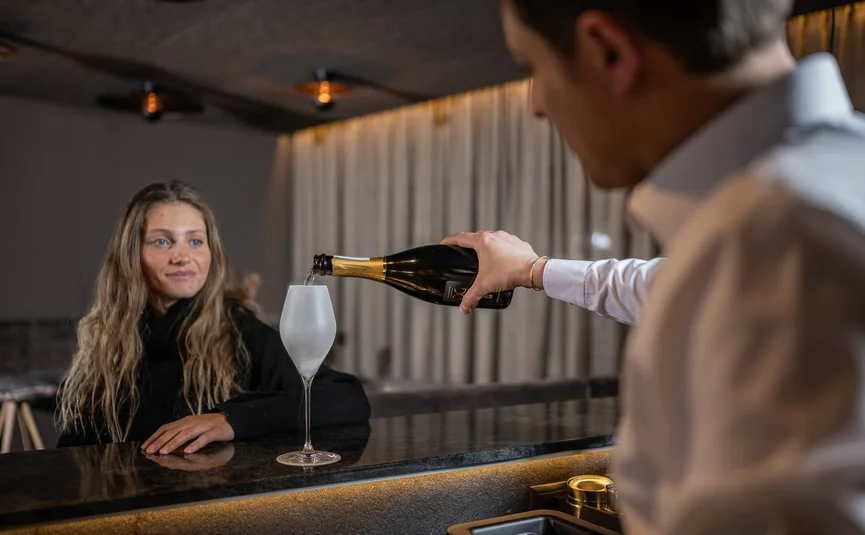 Waiter pouring champagne into glass for woman at bar