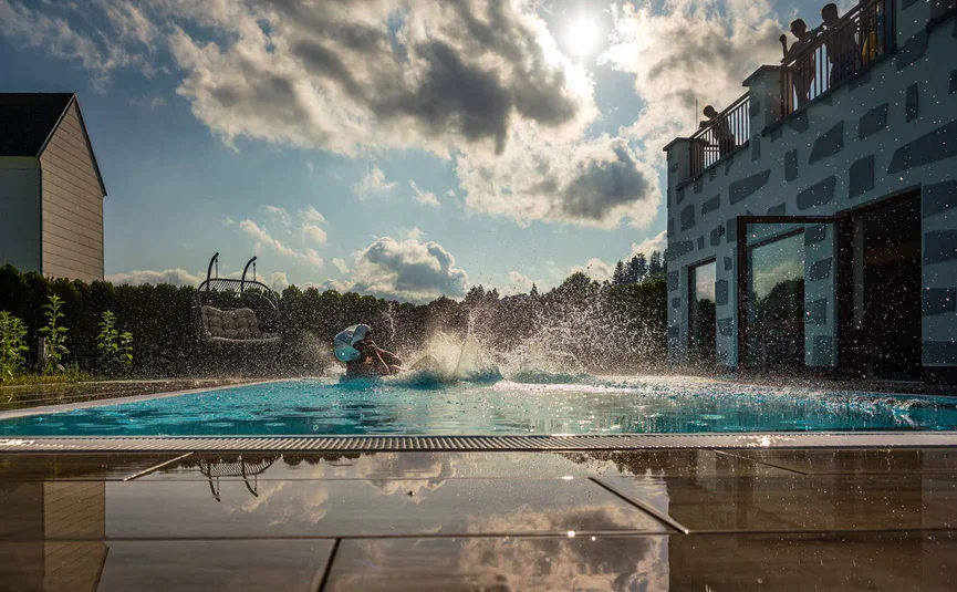 Wohlfühlhotel Rockenschaub **** © Moppetfoto.de Person spritzt im Außenpool vor einem modernen Gebäude, Wolken spiegeln sich auf der Terrasse
