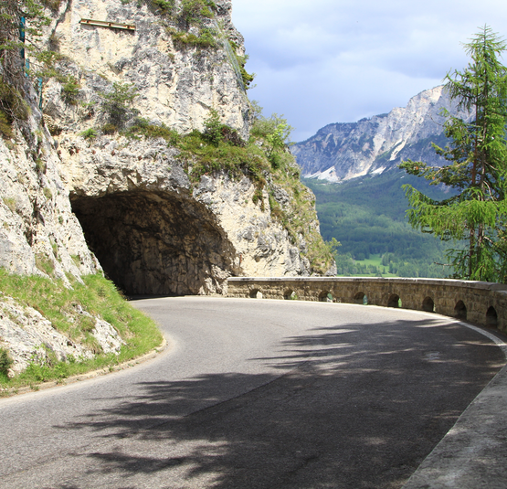 Kurvige Bergstraße mit Tunnel und Felswand in den Alpen