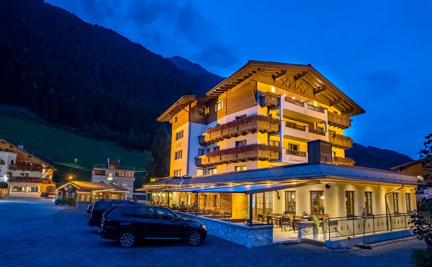 Beleuchtetes Hotel in den Bergen bei Nacht mit geparkten Autos