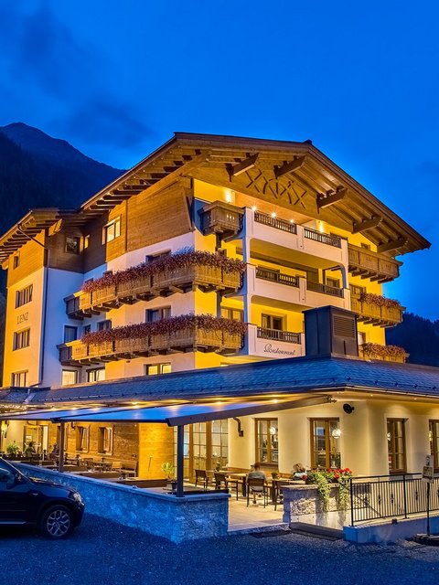 Beleuchtetes Hotel in den Bergen bei Nacht mit geparkten Autos