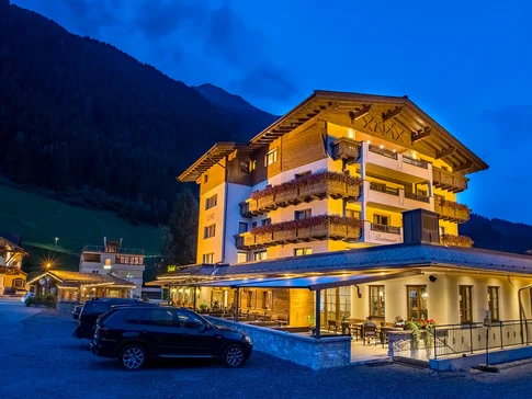 Beleuchtetes Hotel in den Bergen bei Nacht mit geparkten Autos