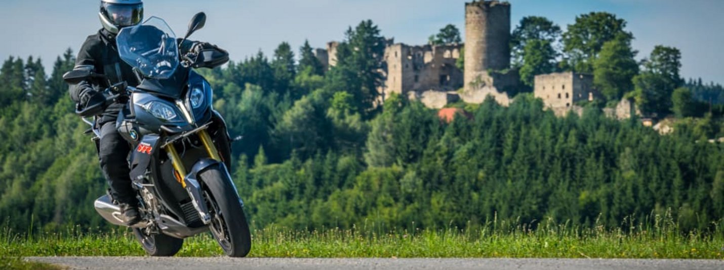 Kurvenreich Motorradwoche 2026 Motorradfahrer auf Straße vor Wald und Burgruine bei klarem Himmel