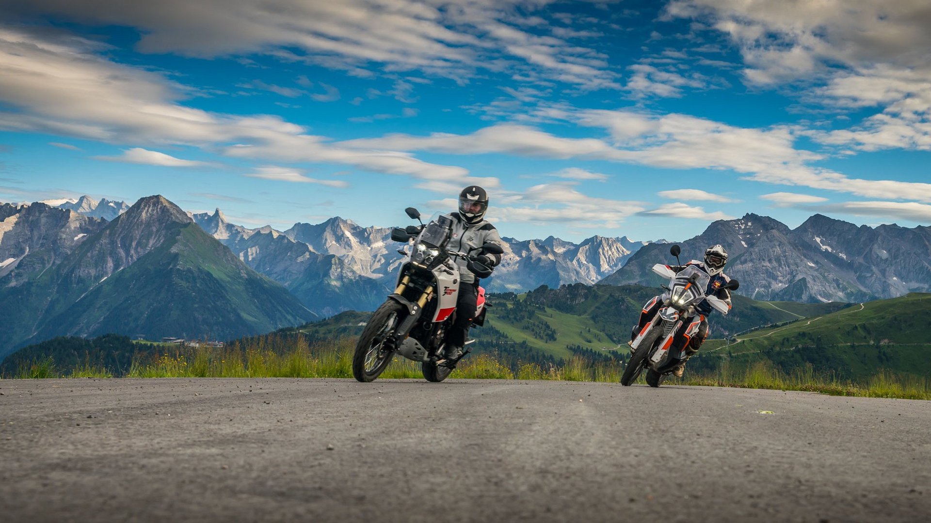 Qualitätsversprechen © Moppetfoto.de Zwei Motorradfahrer auf Bergstraße mit Alpen im Hintergrund bei bewölktem Himmel