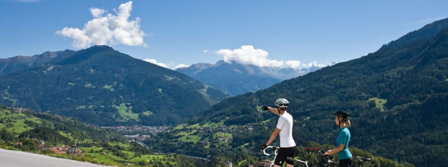 Rein in die Pedale - 7 Nächte Zwei Radfahrer genießen die Aussicht auf grüne Berge und ein Tal bei klarem Himmel