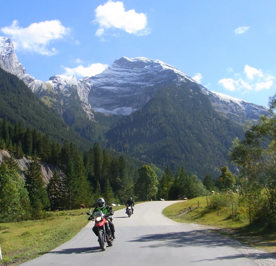 Motorradfahrer auf Straße vor bewaldeten Bergen mit schneebedeckten Gipfeln