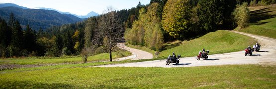 Motorradfahrer auf kurviger Landstraße mit Bergen und Wäldern im Hintergrund