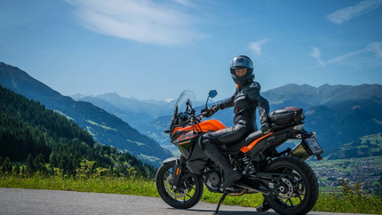 Motorradfahrer in schwarzer Schutzkleidung auf orangefarbener Maschine vor Berglandschaft