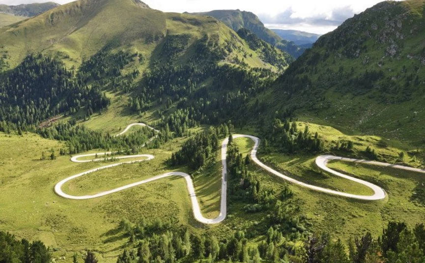 Serpentinenstraße durch grüne Berglandschaft bei Sonnenschein