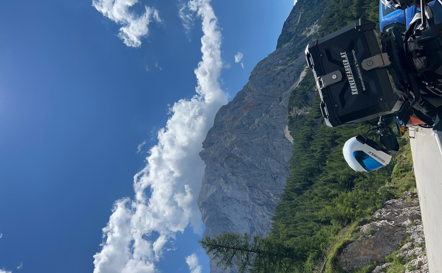 Motorrad mit Koffer vor bergiger Landschaft und blauem Himmel