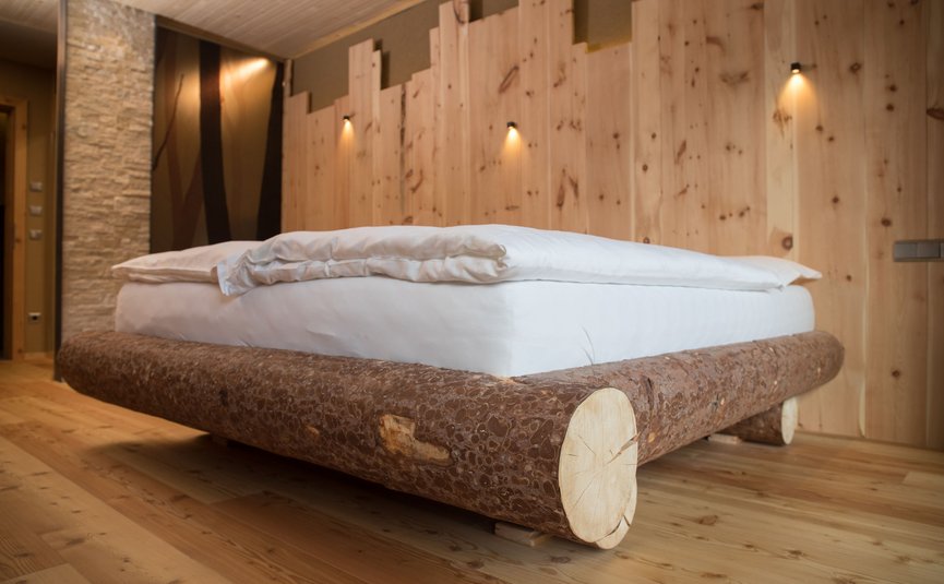 Holzbett aus Baumstämmen mit weißer Bettwäsche in einem Holz-Zimmer