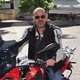 Mann mit Sonnenbrille auf rotem BMW Motorrad auf gepflastertem Platz