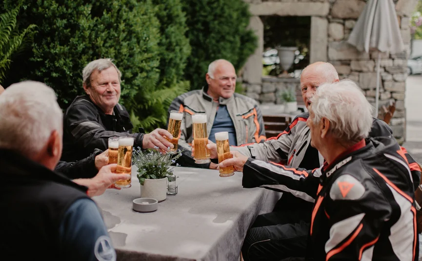 Salzkammergutrunde Ältere Männer in Motorradbekleidung stoßen mit Biergläsern im Garten an