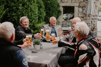 Salzkammergutrunde Ältere Männer in Motorradbekleidung stoßen mit Biergläsern im Garten an