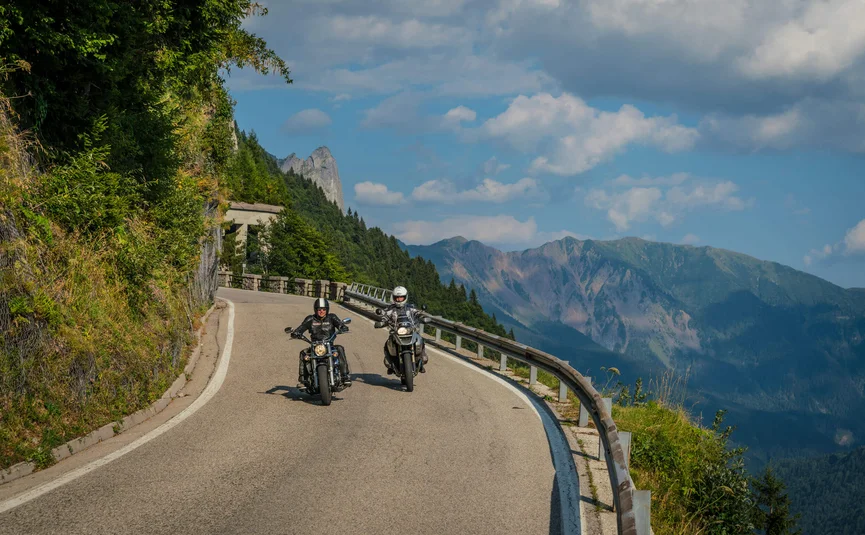 Motorvakantie in Friuli - Carnia © Moppetfoto.de Twee motorfietsers op een kronkelende bergweg met bergen op de achtergrond.
